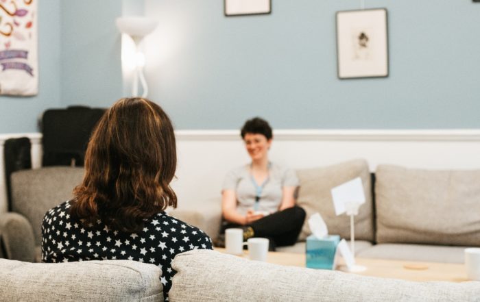 Interior, two women sitting across from each other in a comfy living room, for “FREYA: Helping Women Find Their Way at Kyra”