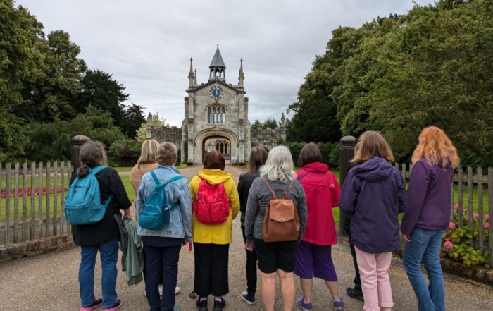 Exterior, several women standing in front of a gothic stone building with their backs turned, for “Taking Steps Toward Better Wellbeing”