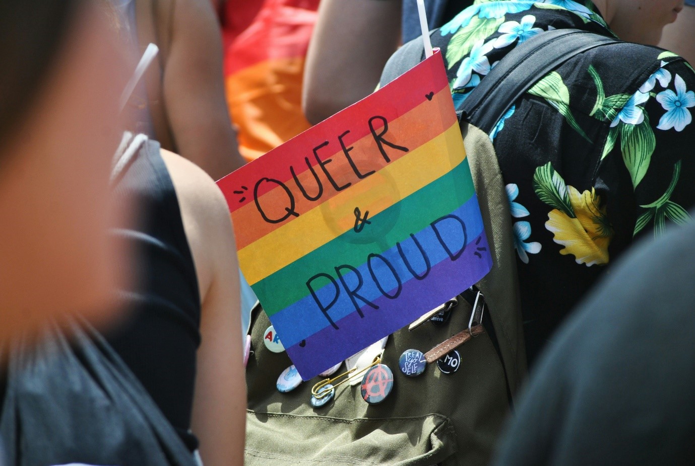 Exterior, a rainbow sign reading ‘Queer and Proud’ hanging out of someone’s backpack, for “A New LGBTQ+ Women’s Group at Kyra”