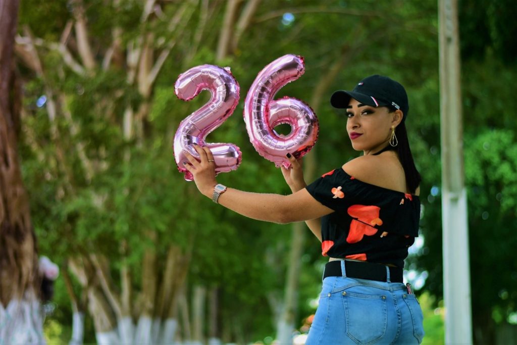 Exterior, a woman holding up inflated ballons with the numbers 2 and 6, for “ROSE+ Is Here for Women Figuring Things Out”