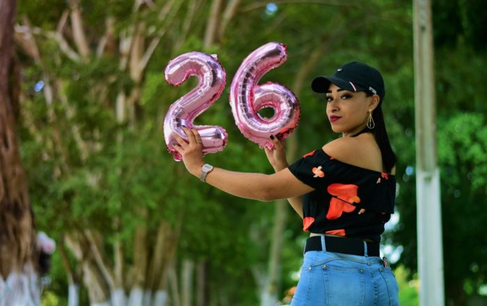 Exterior, a woman holding up inflated ballons with the numbers 2 and 6, for “ROSE+ Is Here for Women Figuring Things Out”