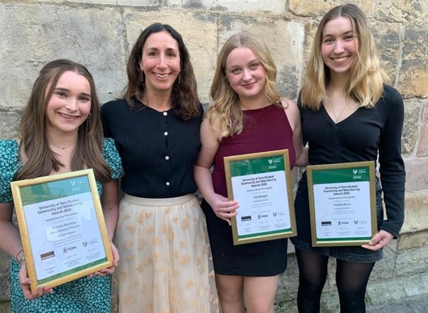 Exterior, four women holding awards outside a stone building, for “Kyra Volunteers Shortlisted for Prestigious University Awards”