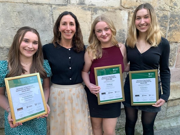 Exterior, four women holding awards outside a stone building, for “Kyra Volunteers Shortlisted for Prestigious University Awards”