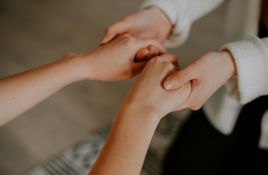 Interior, two women supportively clasping each other’s hands, for “New Monthly Workshop: Exploring the Five Ways to Wellbeing"