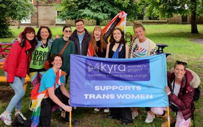 Exterior, a group of people in colourful garb with a banner reading 'Kyra Supports Trans Women', for Kyra at York Pride 2026
