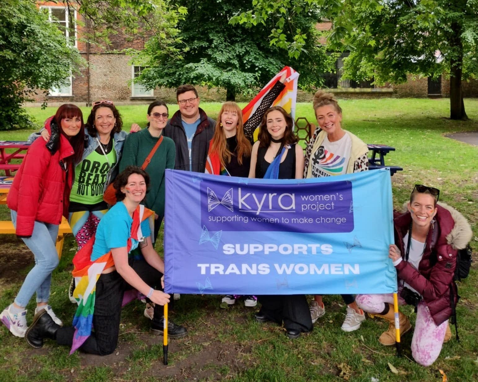 Exterior, a group of people in colourful garb with a banner reading 'Kyra Supports Trans Women', for Kyra at York Pride 2026